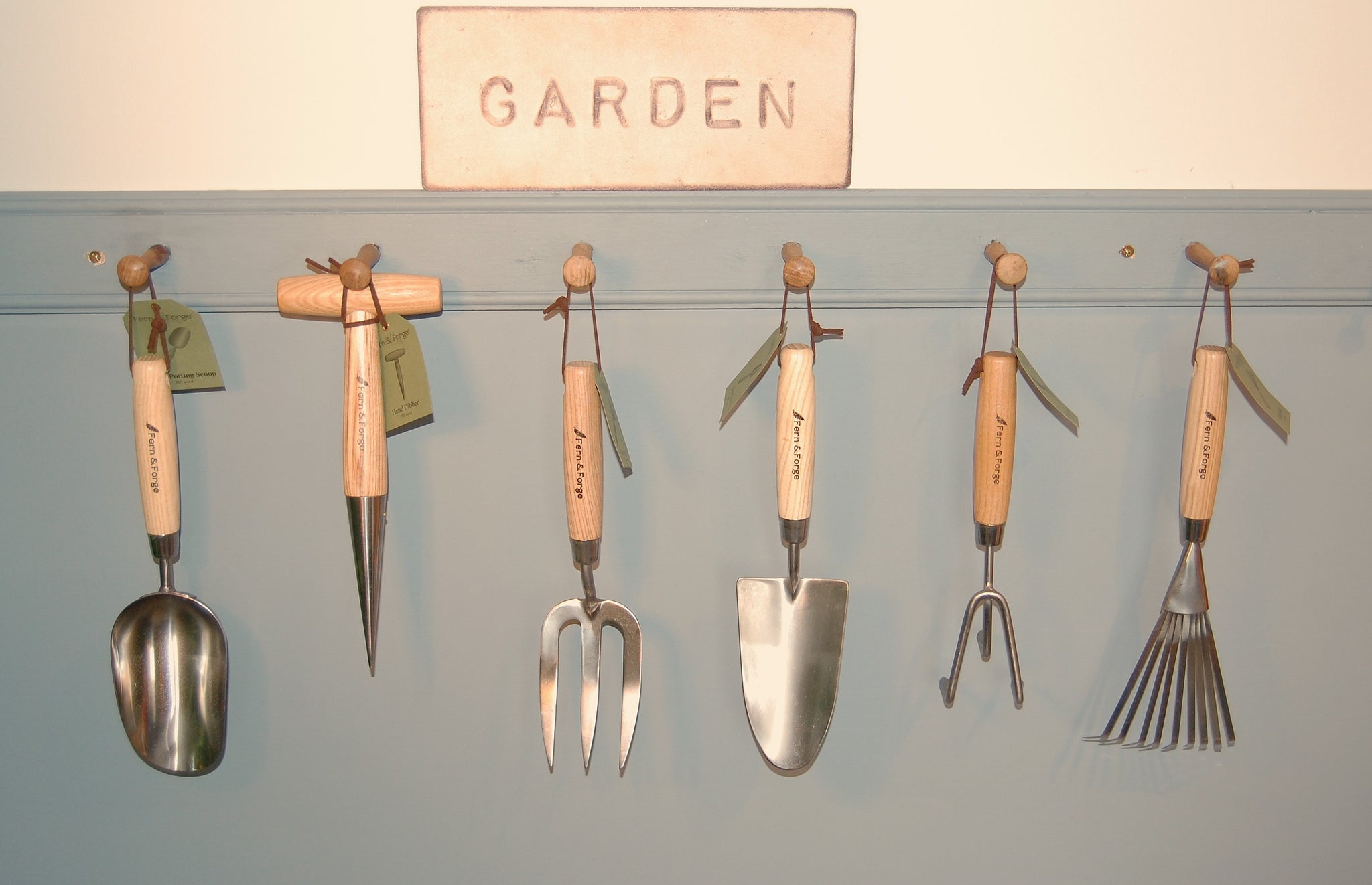 Set of gardening tools hanging on a wall with a sign that says 'Garden'.