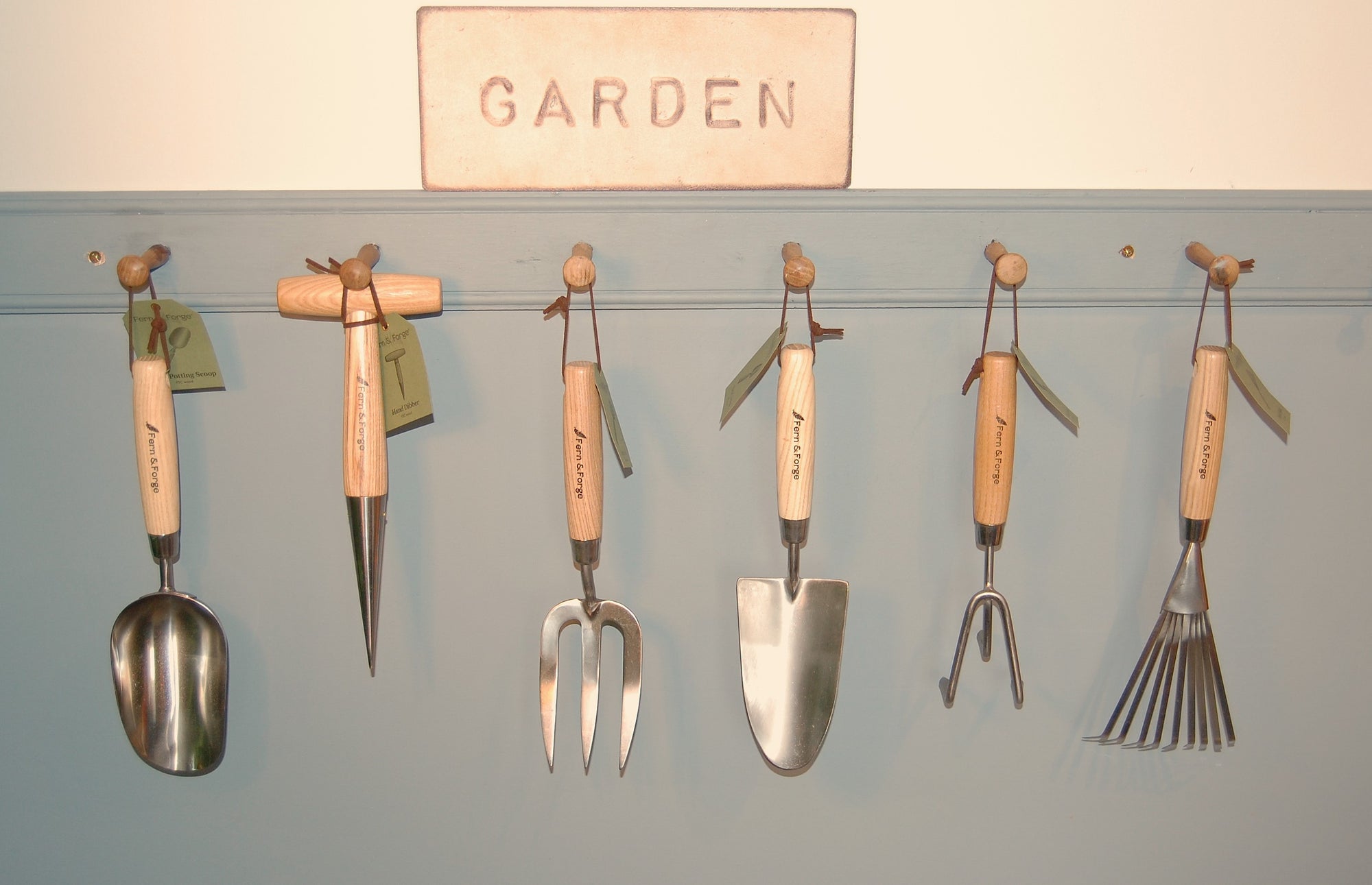 Set of gardening tools hanging on a wall with a sign that says 'Garden'.